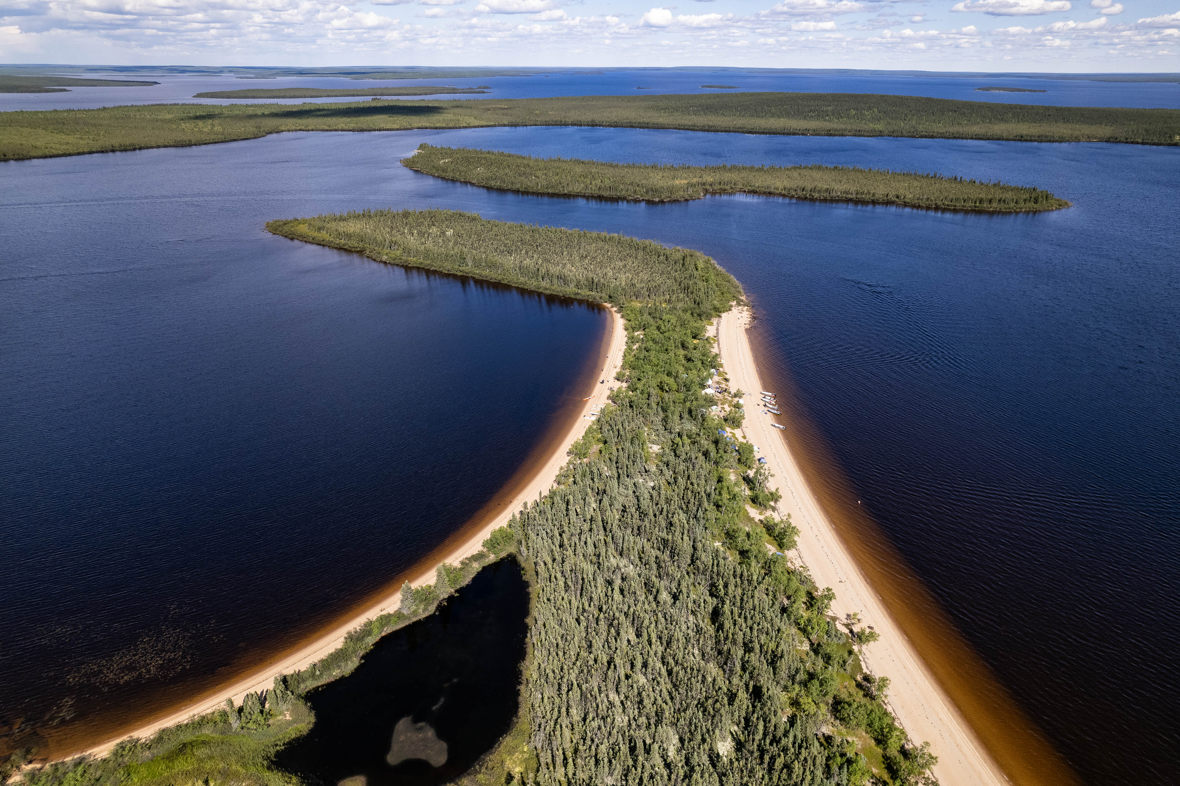 Une vue aérienne d'une pointe de sable recouverte d'arbres avançant dans un cours d'eau foncé.