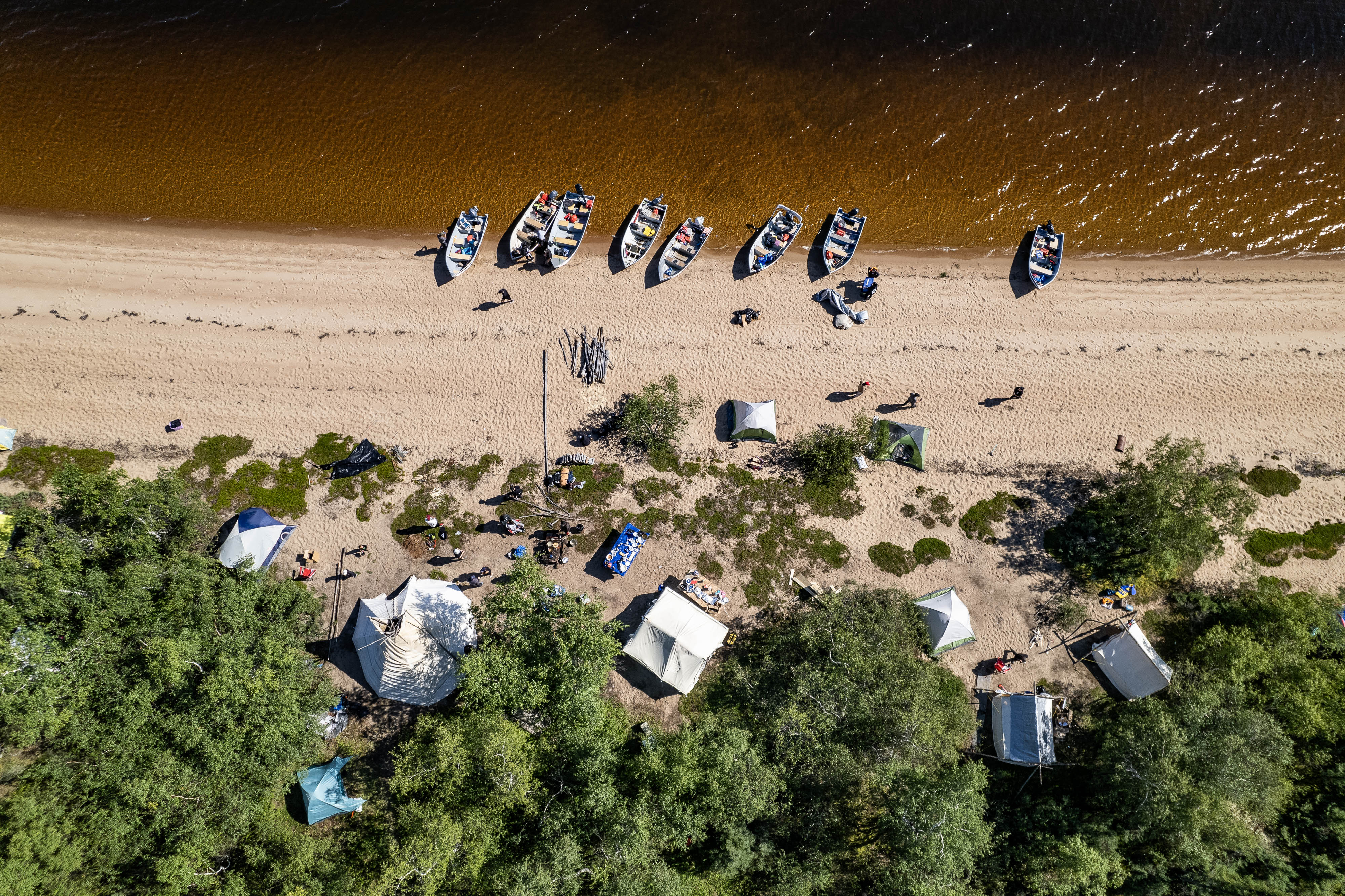 Une vue aérienne de des bateaux, des tentes et des gens au bord d'un cours d'eau.