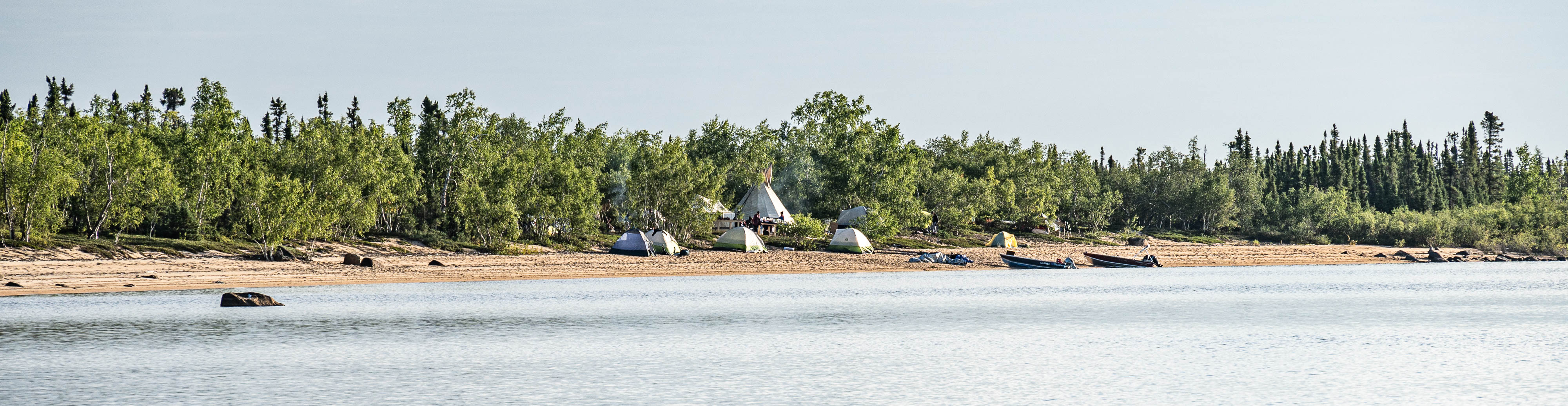 Des bateaux, des tentes et des personnes au bord d'un cours d'eau.