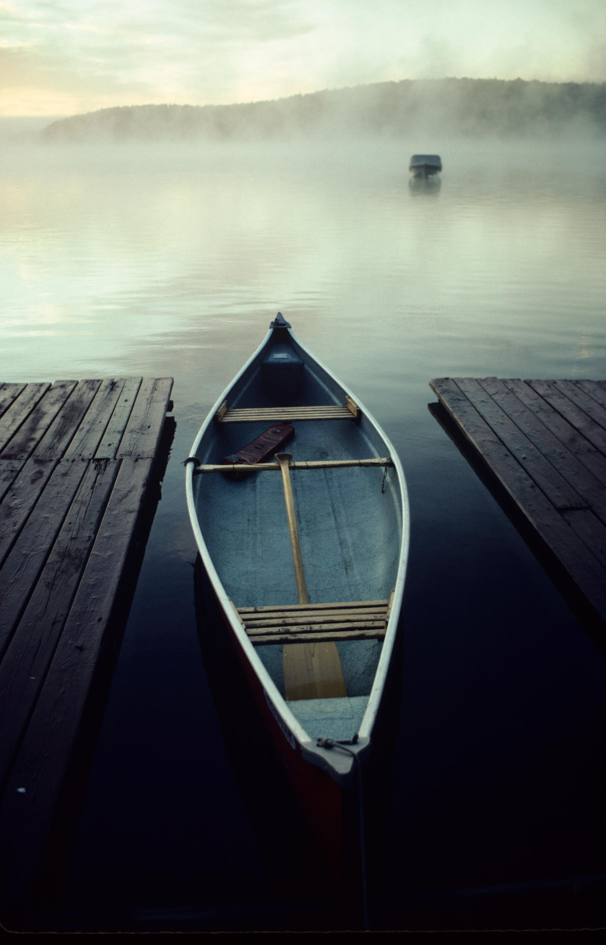 Un canot attaché à un quai sur une rivière brumeuse.