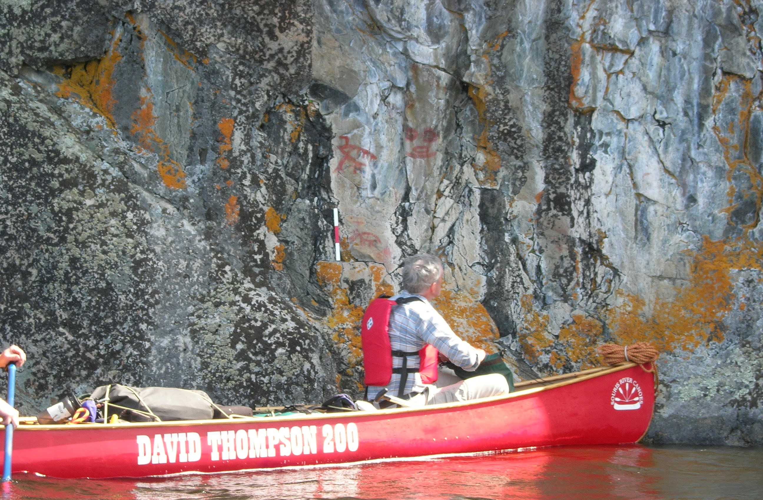 Des personnes en canot s'arrêtent pour observer des pictogrammes le long d'une paroi rocheuse.