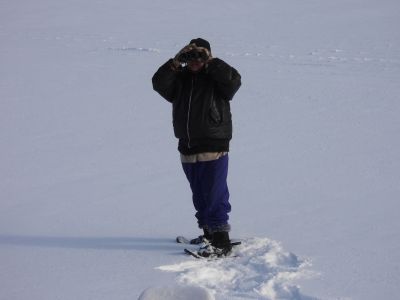 A person standing in the snow, looking into binoculars. / Une personne debout dans la neige regardant dans des jumelles.