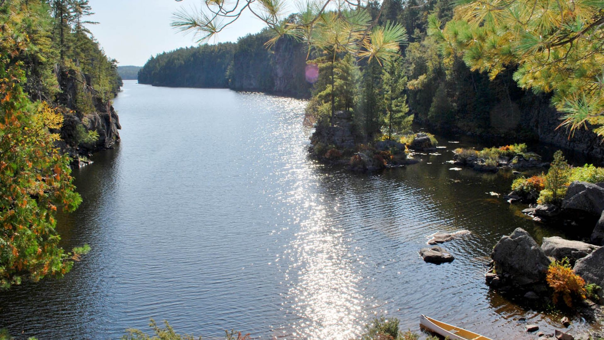 A canoe rests on the shores of the Mattawa River with the sun reflecting off the waters 