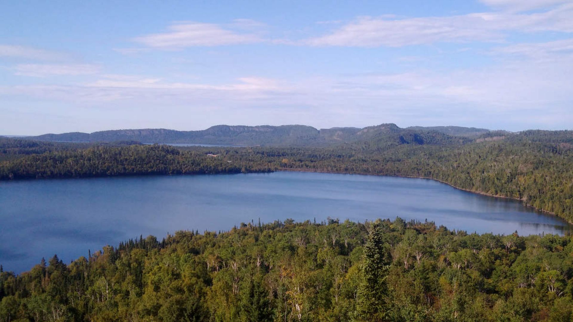 A panoramic view from the Finger Point Lookout. In the foreground is the calm bay of Lake Superior, and in the background are rugged, tree-covered cliffs.