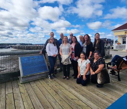 Group of people standing on a boardwalk beside a commemorative plaque.