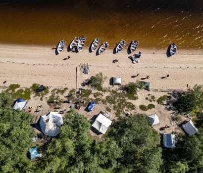 Une vue aérienne de des tentes, des gens et des bateaux sur la plage au bord de l'eau.